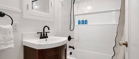 A bathroom with a white sink, dark wooden cabinet, and a white bathtub.
