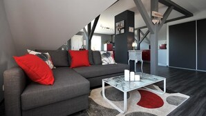 A modern living room with a grey sectional sofa, red cushions, a glass coffee table, and a unique ceiling design.
