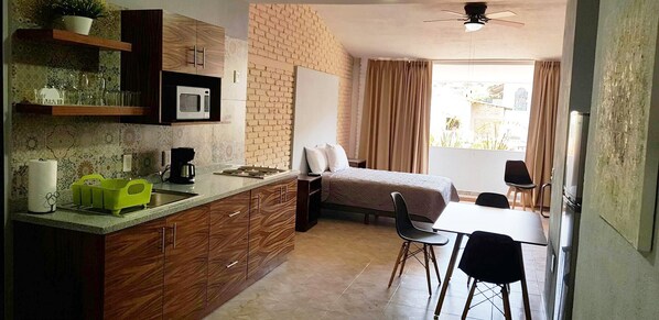 A compact hotel room with a kitchenette, a bed, a dining area, and a view of the outdoors.