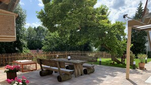 Eine Terrasse im Freien mit einem Holztisch und Bänken, umgeben von einem Holzzaun und Topfpflanzen.