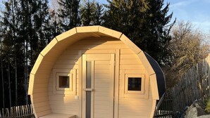 Eine hölzerne, rund geformte Hütte mit einer zentralen Tür, zwei kleinen Fenstern und einer Bank davor.