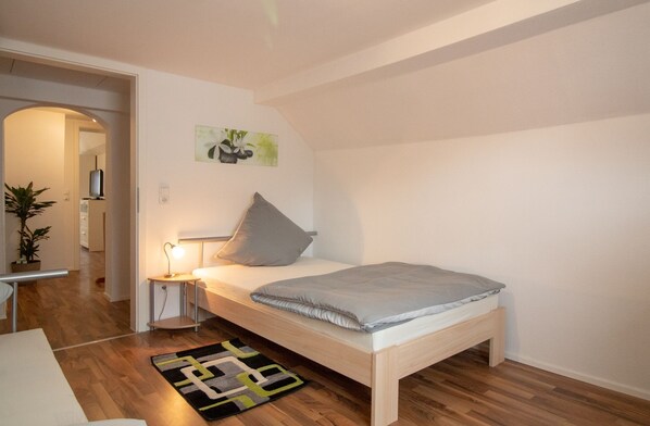 Ein Schlafzimmer mit einem Einzelbett, einem Nachttisch mit Lampe, einem kleinen Teppich und einem Bild an der Wand.
