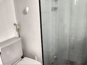 Un baño con inodoro, ducha con puerta de cristal y pared blanca.