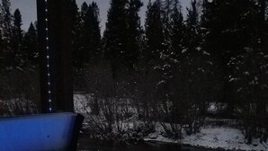 A hot tub with a blue light, surrounded by snow-covered ground and trees. - The Ultimate Outdoor Adventure with Indoor Comfort (Darby)