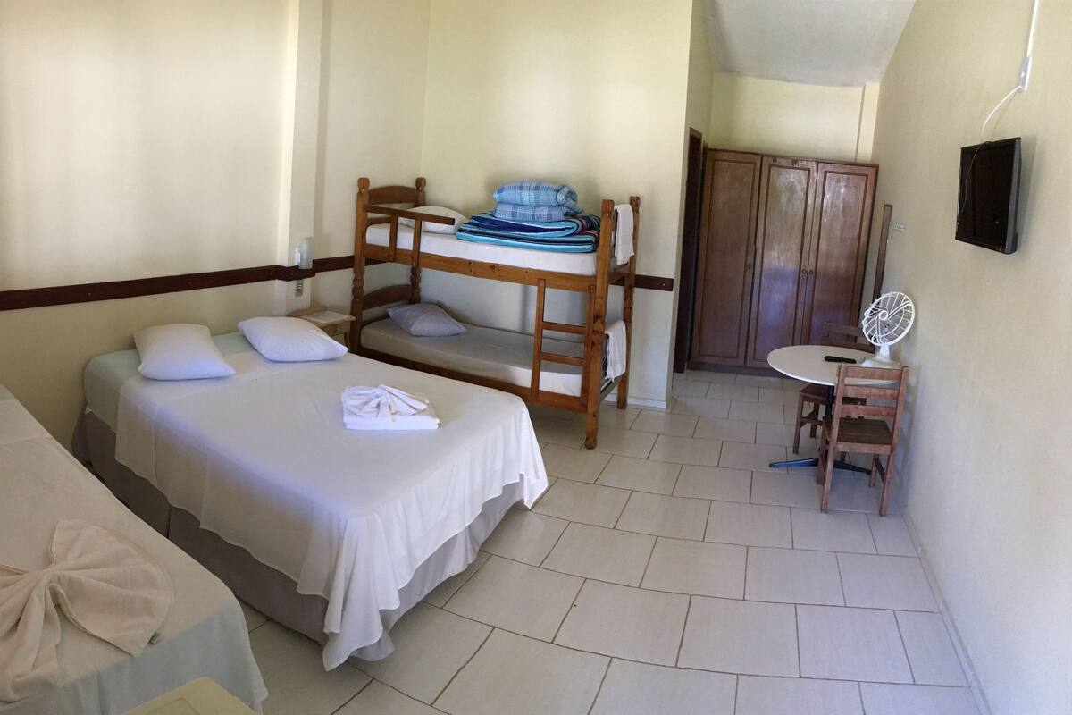 A room with two single beds, a bunk bed, a small table with a fan, and a wooden wardrobe.