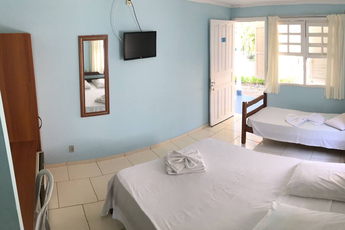 A bedroom with two beds, a TV, and a window with curtains.