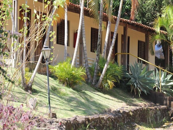 A building with a tiled roof, surrounded by palm trees and various plants. - Big Valley Hotel Fazenda (Monte Alegre do Sul)