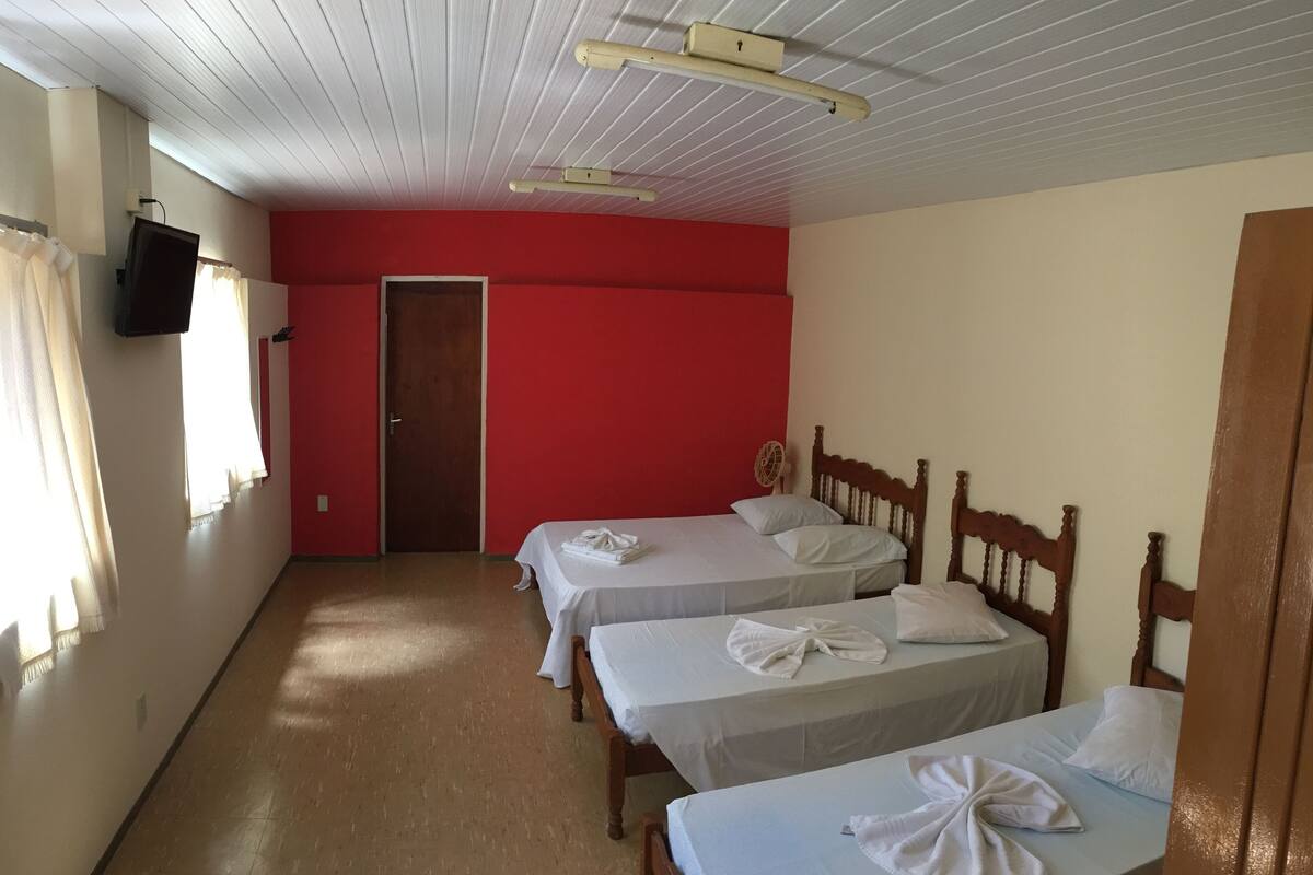 A room with two beds, a television, a door, and a ceiling fan.