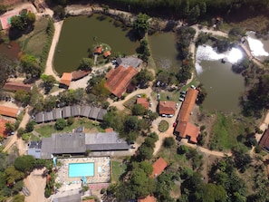 An aerial view of a residential area with multiple ponds, a swimming pool, and houses with red-tiled roofs. - Big Valley Hotel Fazenda (Monte Alegre do Sul)