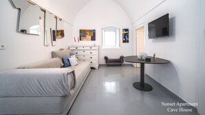 A modern bedroom with a bed, dresser, and a small table with a lamp. There is a TV mounted on the wall and artwork on the walls.