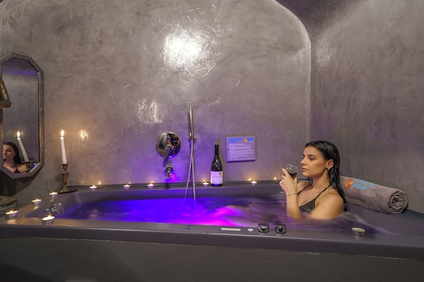 A spa bath with candles, a wine bottle, and a towel.