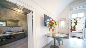 Une cuisine moderne dotée d’un grand îlot central, d’un coin repas avec une table en verre et d’un couloir menant à une véranda.