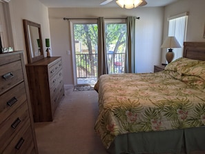 Quarto com cama, cómoda de madeira e vista para o exterior através de uma porta deslizante.