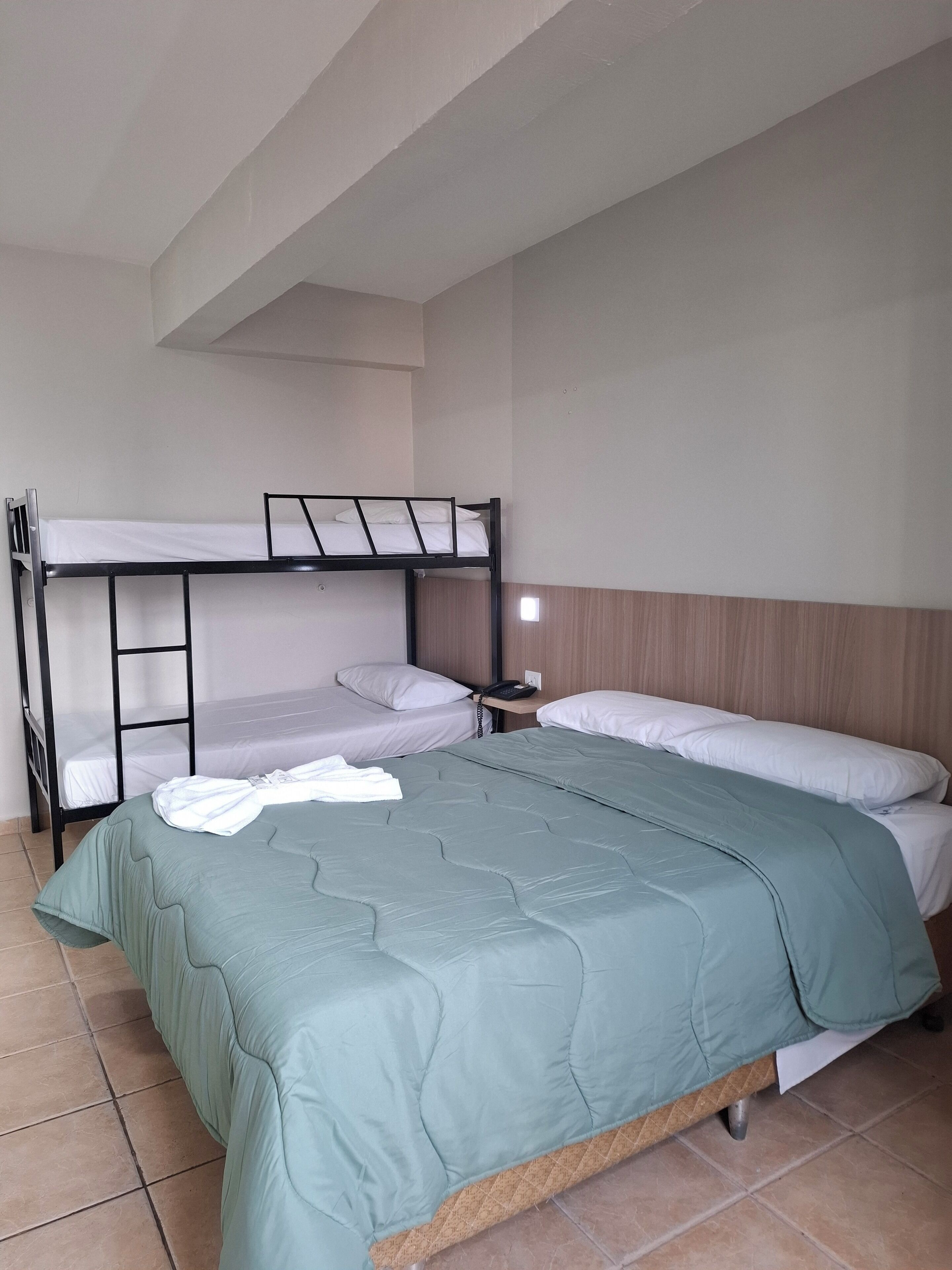 A room with a bunk bed, a single bed, and a bedside table with a phone.