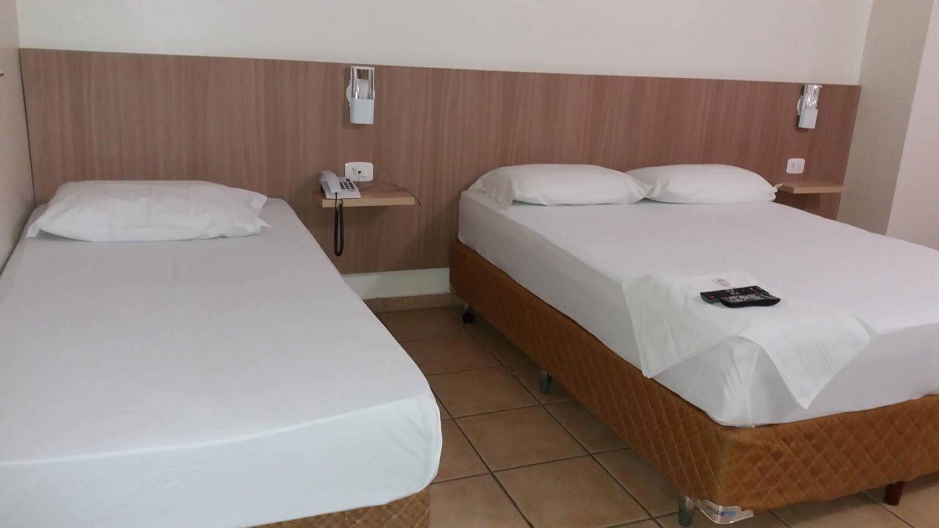 Two single beds with white linens, wooden headboards, bedside tables with lamps, and a remote control on the right bed.