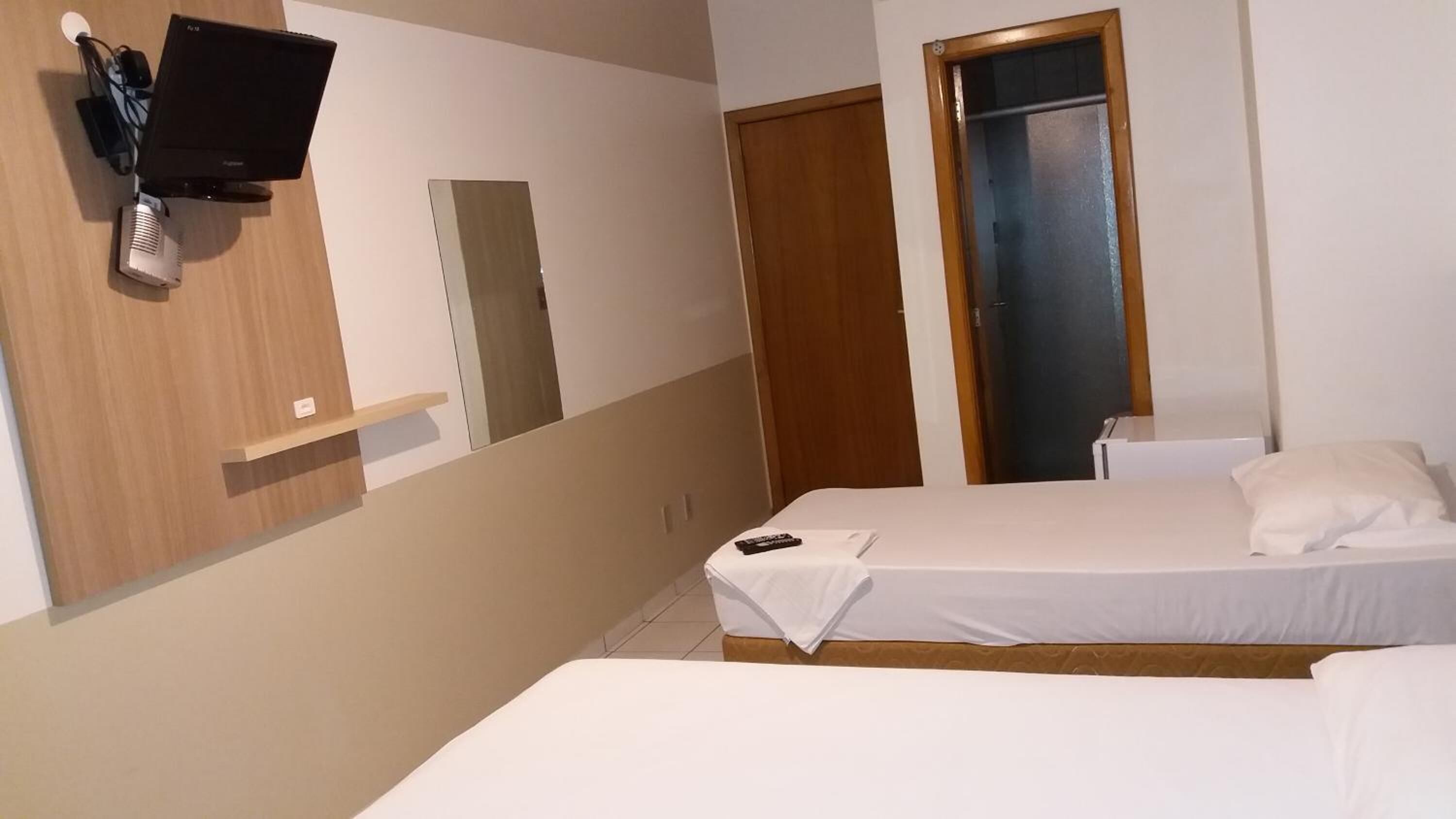 A bedroom with two beds, a TV mounted on the wall, and a wardrobe.