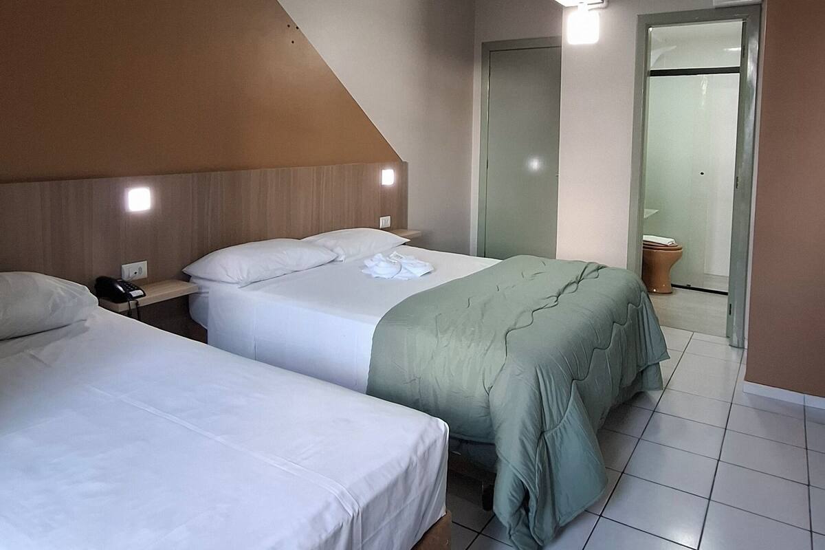 Une chambre d’hôtel avec deux lits, un sol carrelé, une tête de lit en bois et une porte de salle de bain visible.