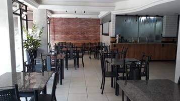 Uma sala de jantar moderna com várias mesas e cadeiras, uma parede de tijolos e uma área de cozinha com uma janela grande.