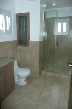 A bathroom with a toilet, a glass-enclosed shower, and a wooden cabinet. - Casa Lila (Montecristi)