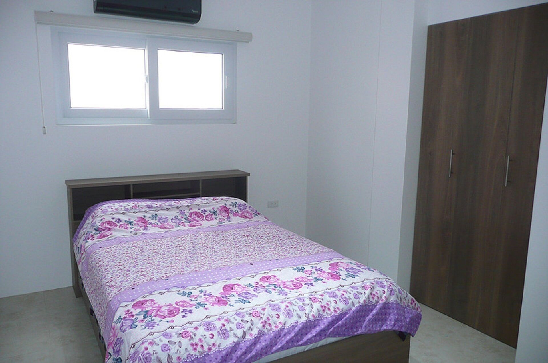A bedroom with a bed, a window, and a wardrobe.