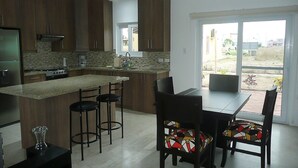 A modern kitchen with dark wooden cabinets, a granite countertop, a built-in stove, and a dining area with a table and chairs. - Casa Lila (Montecristi)