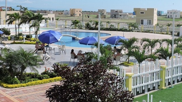A resort pool area with multiple umbrellas, palm trees, and a clear view of the surrounding buildings. - Casa Lila (Montecristi)