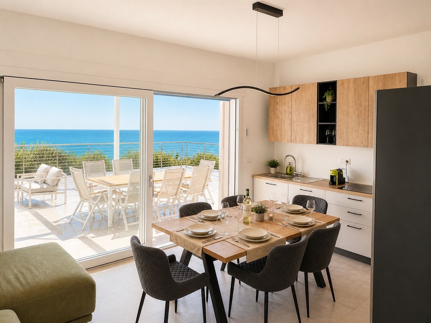 A modern kitchen with a view of the sea, a dining area with chairs and a table, and a large sliding glass door.