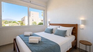 Une chambre avec une grande fenêtre, un lit doté d’une tête de lit en bois et une table de chevet.