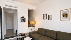Un salon moderne avec un canapé, deux petites tables, une lampe sur pied et des œuvres d’art murales.