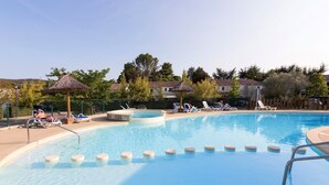 Une piscine entourée d’une clôture et d’arbres, avec des chaises longues et des parasols.