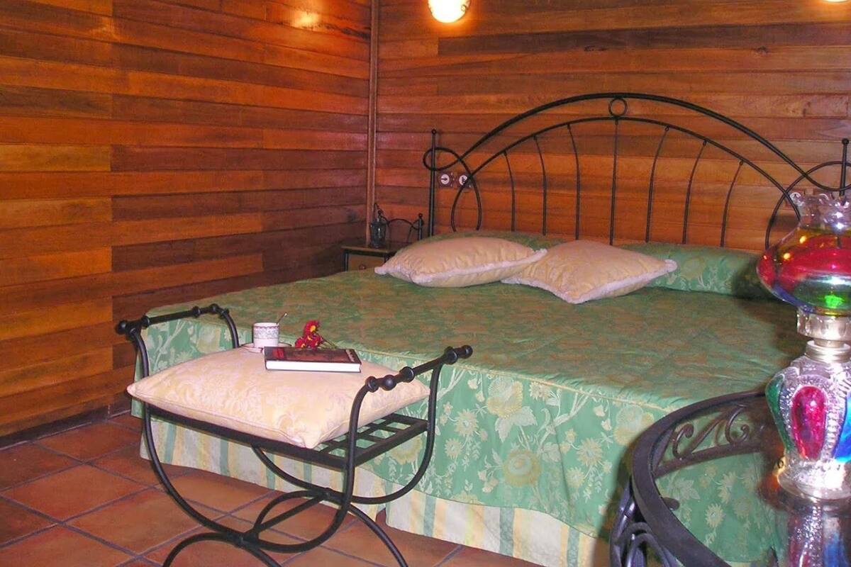 Una habitación de madera con una cama, una mesita de noche, una silla y una mesa con una lámpara.