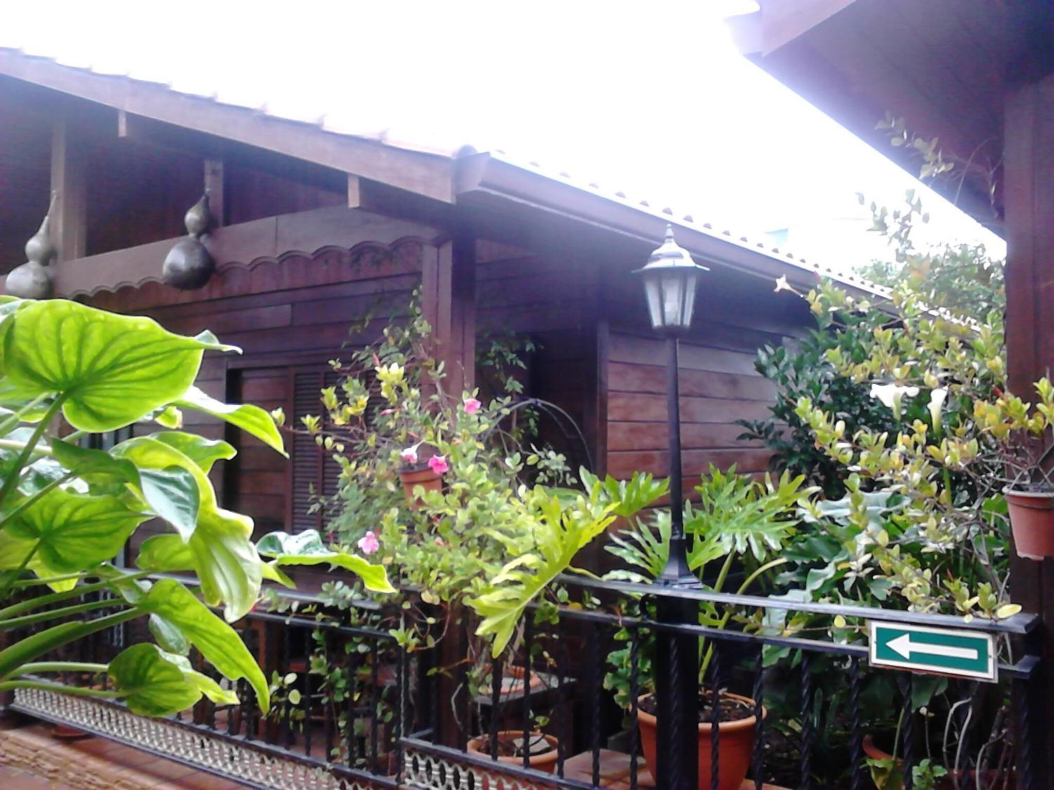 A wooden building with a balcony, potted plants, and a directional sign.
