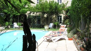 Une maison en pierre avec une piscine, entourée d’une végétation luxuriante et de cactus.