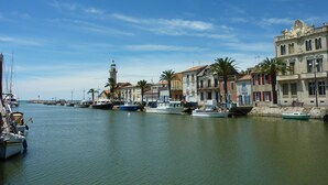 Un port de plaisance avec des bateaux amarrés, un phare et des bâtiments dotés de balcons et de volets rouges.