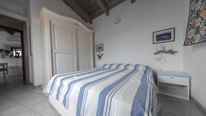 Un dormitorio con una cama, un escritorio y una silla. Hay una puerta que da a un baño y una cocina.