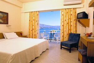 A hotel room with a bed, a chair, a small table with chairs, a television, and a view of the sea.