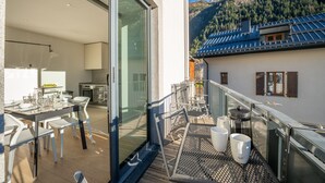Et moderne køkken med spiseplads, en balkon med udendørs møbler og udsigt til et bjerglandskab.