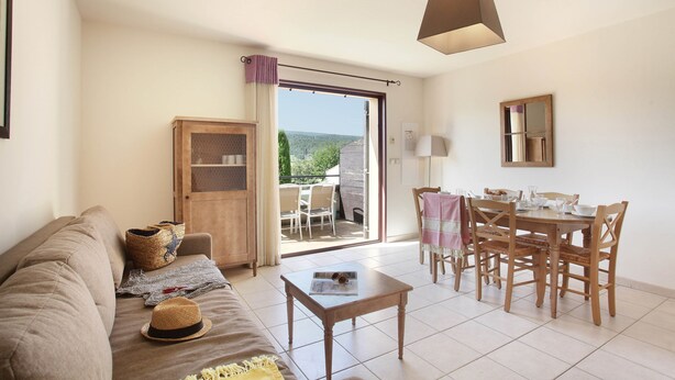 Una sala de estar con un sofá, una mesa de centro, una mesa de comedor con sillas, un aparador de madera y vistas a un espacio exterior a través de una puerta de cristal.