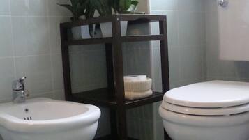 Un baño con bidé, inodoro y una estantería de madera con una planta.