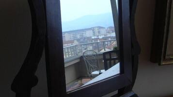 A view from a balcony with a metal railing, overlooking a cityscape with buildings and mountains in the distance.