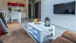 A modern living room with a white brick wall, a flat-screen TV, and a wooden coffee table with fruit. - Apartamenty hoteLOVE pod Debami (Karpacz)