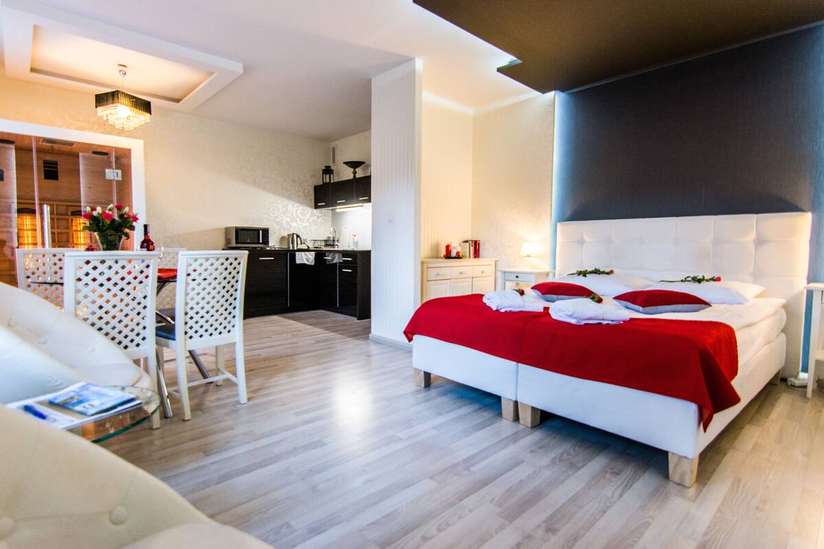 A modern hotel room with a large bed, a dining area, and a kitchen.