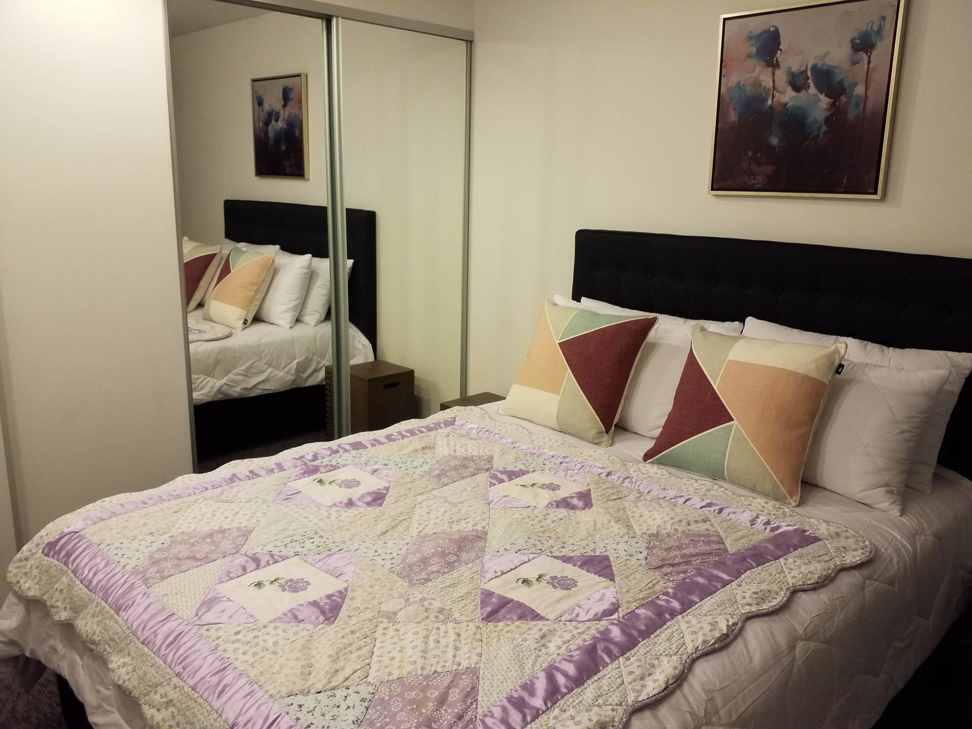 A neatly made bed with a patterned quilt, a black headboard, and several pillows.