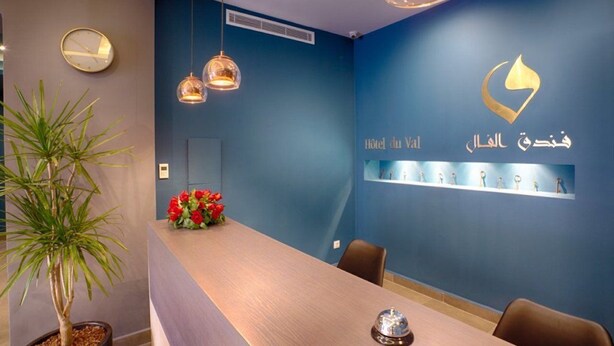Un espace d’accueil avec un mur bleu, un comptoir de réception en bois, une plante en pot, une horloge et une étagère ornée d’objets décoratifs.