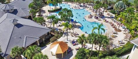 An aerial view of a resort with a large central pool, surrounded by palm trees and lounge areas.