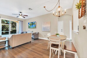A modern living room with a sofa, a dining table with chairs, a ceiling fan, and artwork on the walls. - Magnolia Style Condo at Windsor Hills with Disney Theme Bunk Room (Kissimmee)