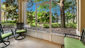 A covered patio with two rocking chairs and a bench, overlooking a landscaped garden with trees and shrubs. - Magnolia Style Condo at Windsor Hills with Disney Theme Bunk Room (Kissimmee)