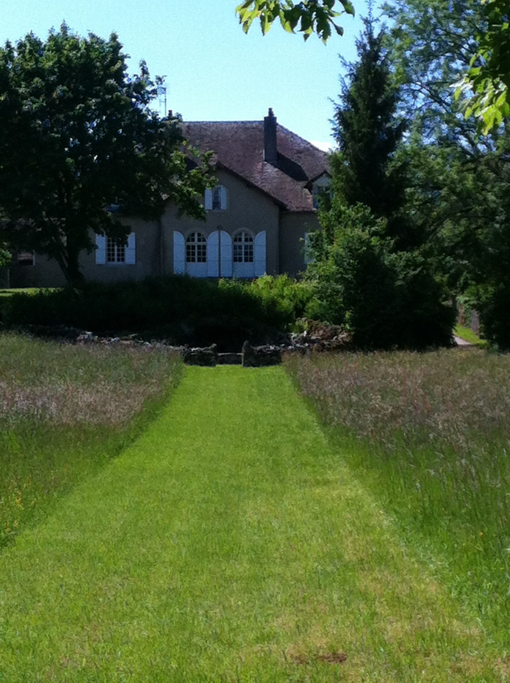 A house with a paved driveway leading to a front door, surrounded by trees and a well-maintained lawn.
