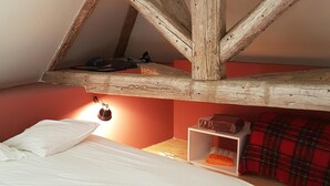 A bedroom with a sloped ceiling, a bed, a shelf with items, and a red wall. - Beautiful view of Baume les Messieurs (Baume les Messieurs)