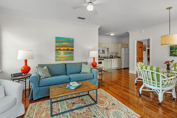 A living room with a blue sofa, a coffee table, and a dining area with a wicker chair. - Charlotte at Jubilee Suites Bed & Breakfast. 1K/1B (Fairhope)